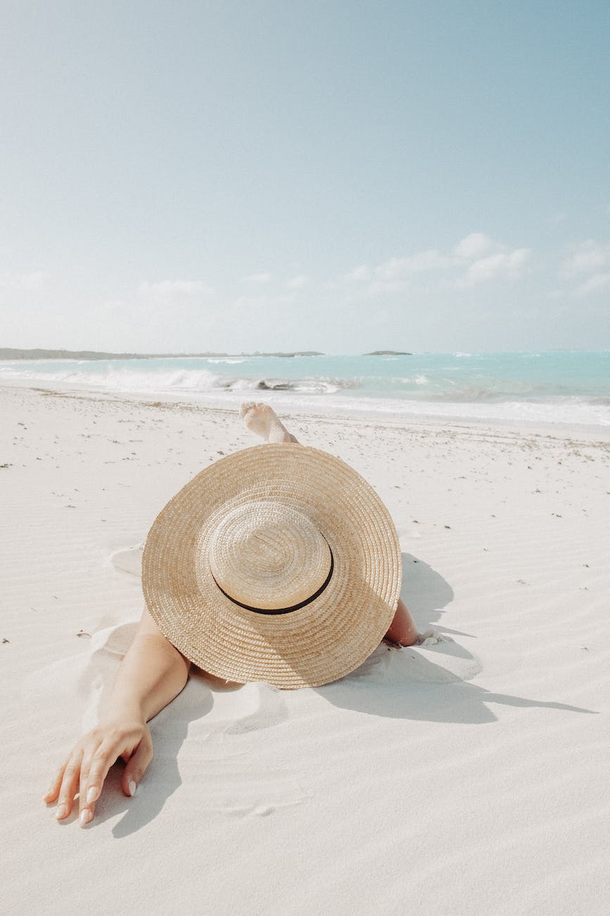 unrecognizable woman in hat lying on beach